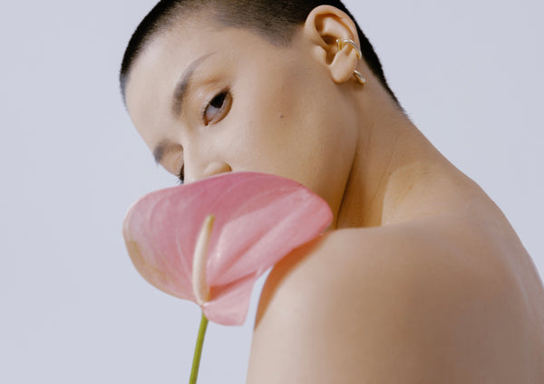 Girl with shaven head holding pink flower for spring | OneNightOnly