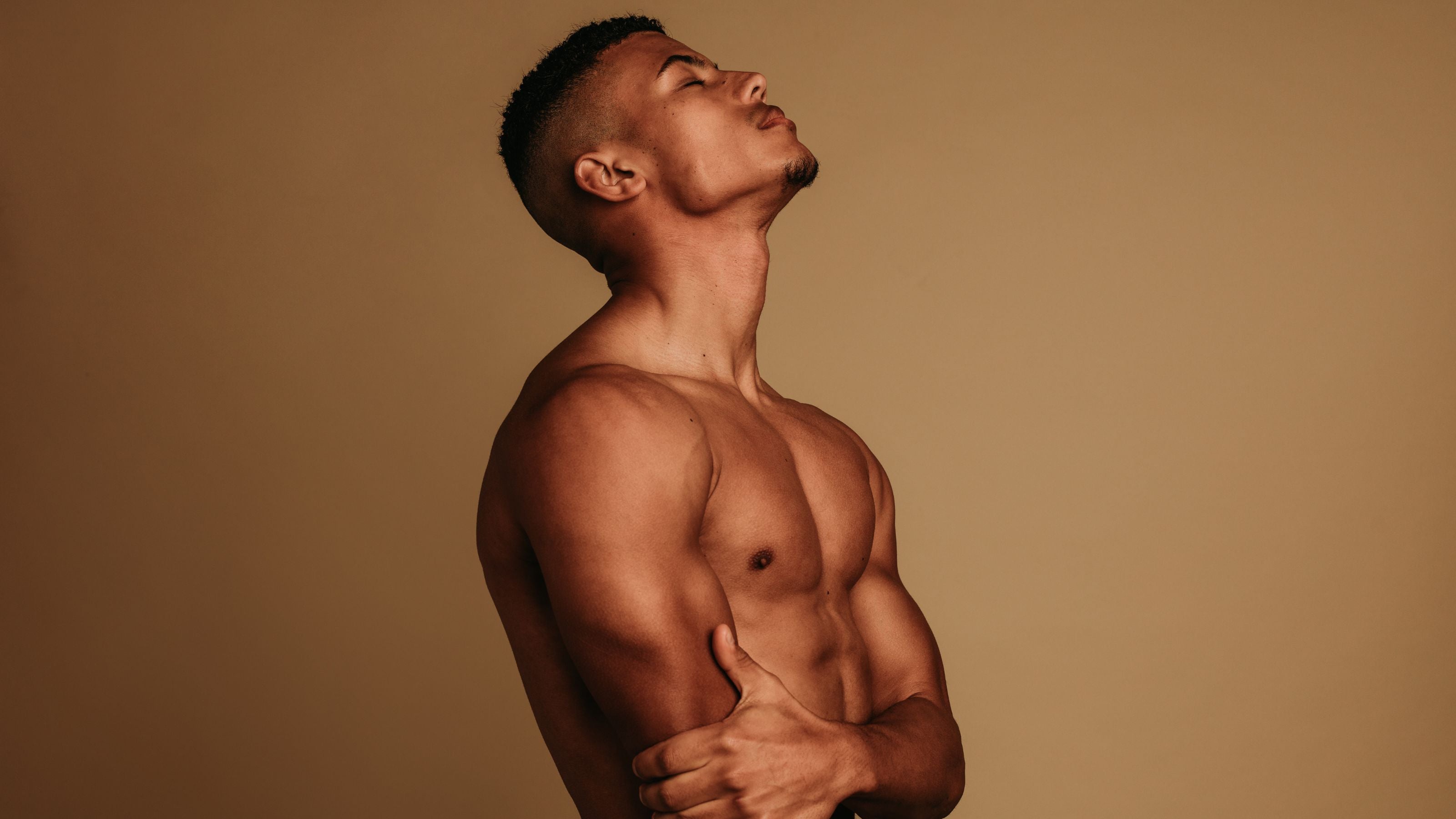 Male model with abs posing topless in front of a nude background for Movember & Men's Health Awareness Month