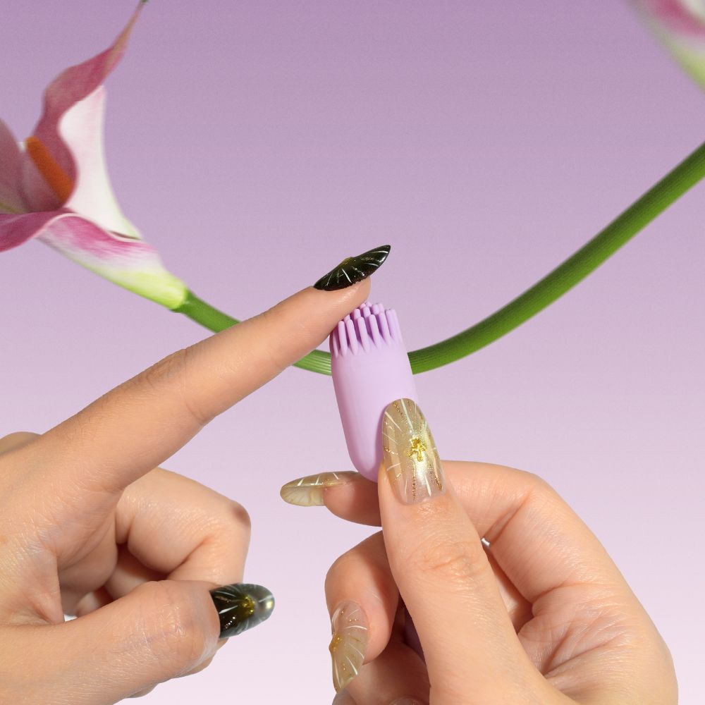 Close-up of the brush-tip end of Svakom Plume Interactive Brush Tail Bullet Vibrator being touched with a fingertip, with flowers in the background.
