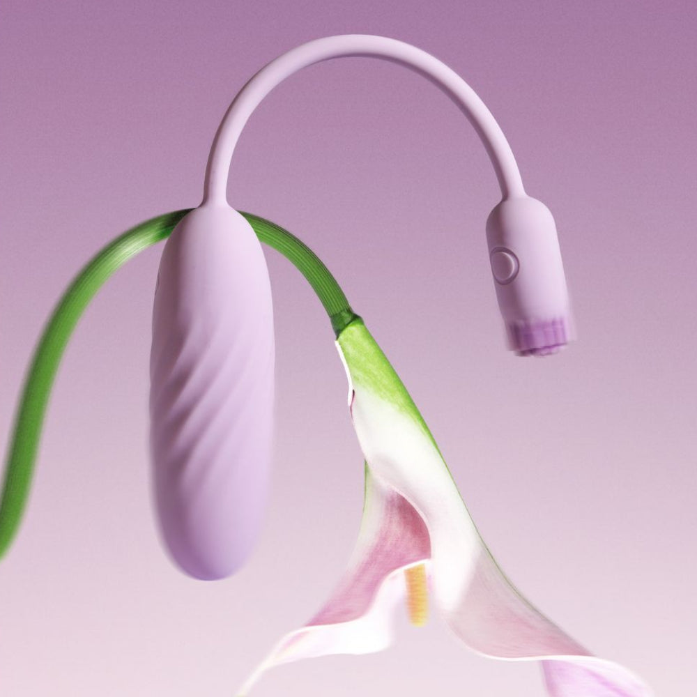 Svakom Plume Interactive Brush Tail Bullet Vibrator in pastel lilac displayed with a flower on a lilac background, showing the flexible tail, bullet body and brush-tip end in motion.