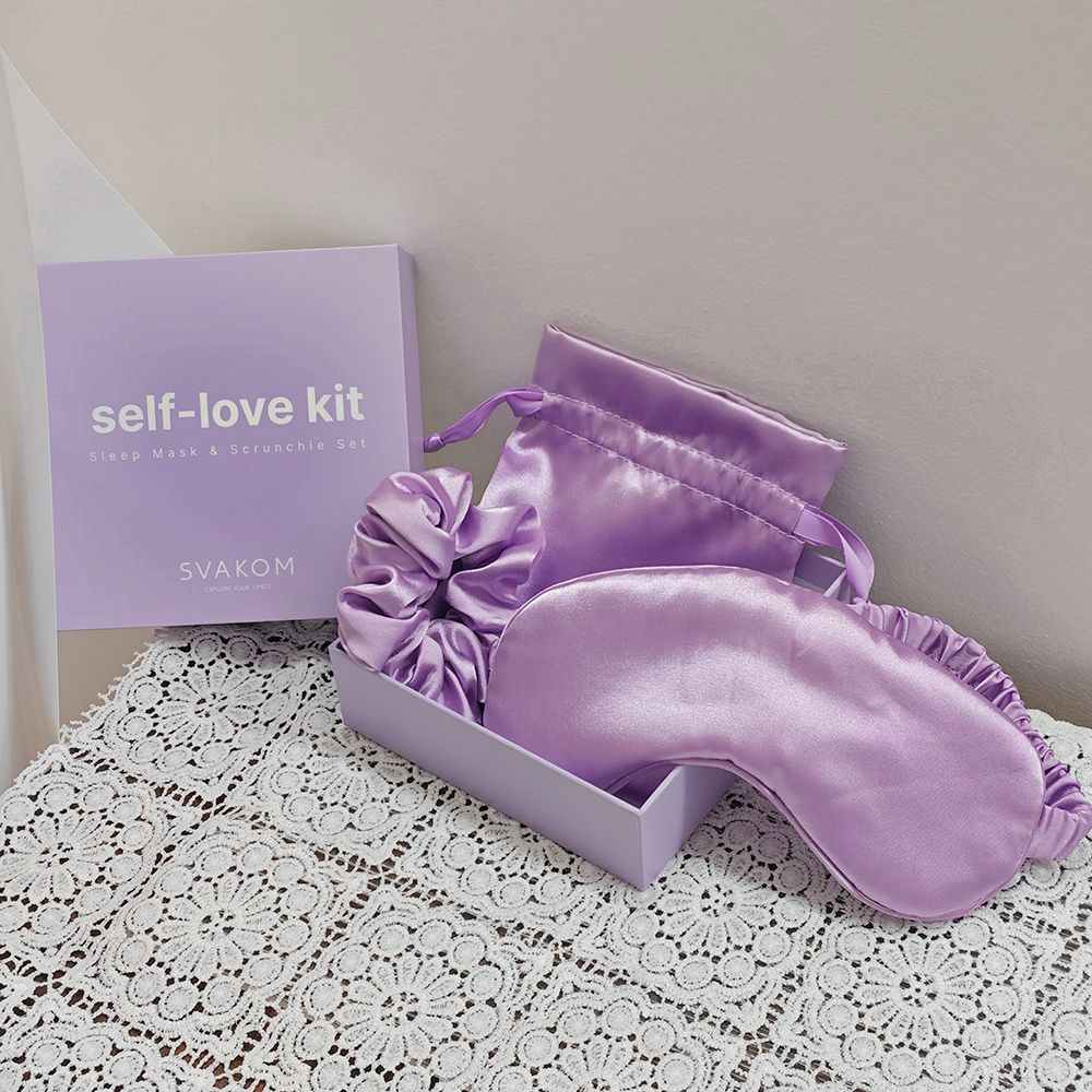 Violet Svakom Self-Love Kit featuring the satin sleep mask, matching satin scrunchie and satin storage pouch arranged inside the open gift box, styled on a white lace surface against a neutral beige background