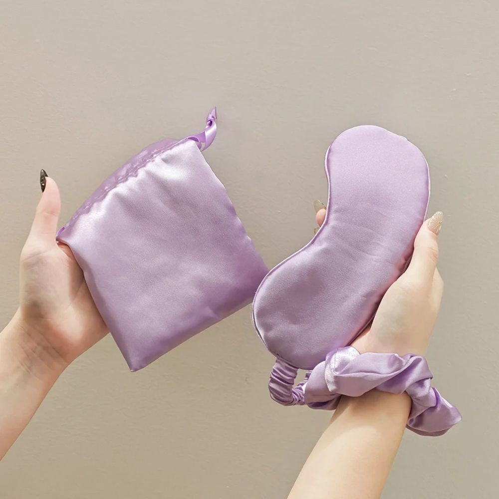 Violet Svakom Self-Love Kit satin storage pouch and contoured sleep mask held in hand, with the matching satin scrunchie worn around the wrist, set against a neutral beige background