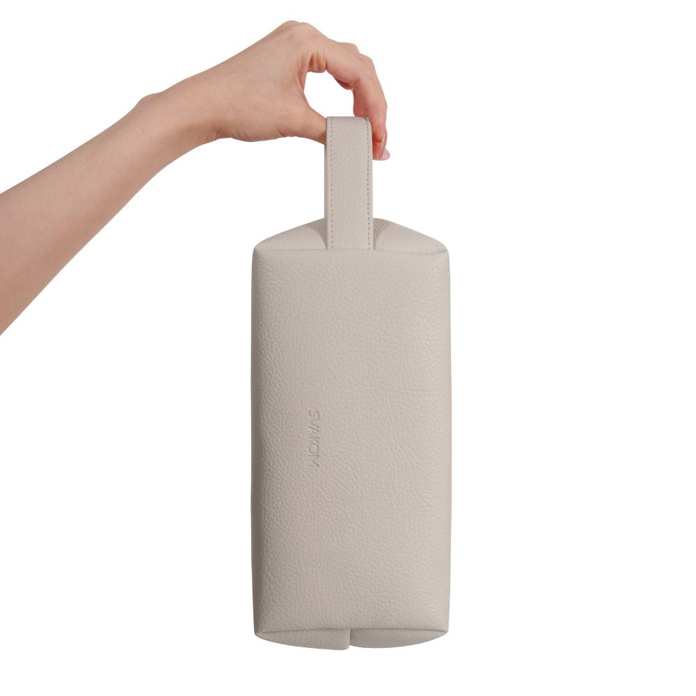 Side view of the Svakom | Vegan Leather Storage Bag with Carry Handle (Beige) held vertically by the carry handle, featuring the embossed 'SVAKOM' logo on a plain white background