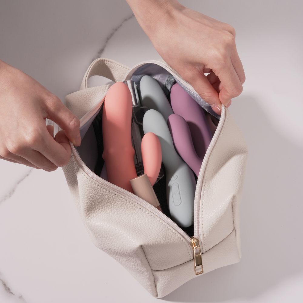 Open Svakom | Vegan Leather Storage Bag with Carry Handle (Beige) filled with pink, grey and purple vibrators, held open by both hands on a light marble surface