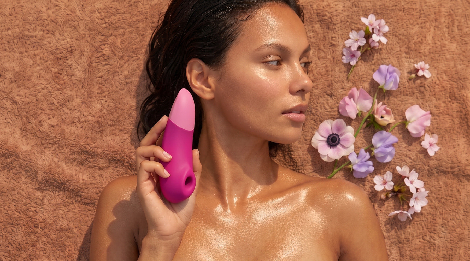 Female model lying on her back with a Womanizer adult toy in her hand and Spring flowers scattered next to her head for Spring