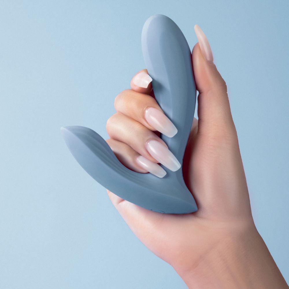 Hand holding Svakom | Erica App-Controlled Wearable Vibrator & Anal Stimulator (Dusty Blue) on blue background