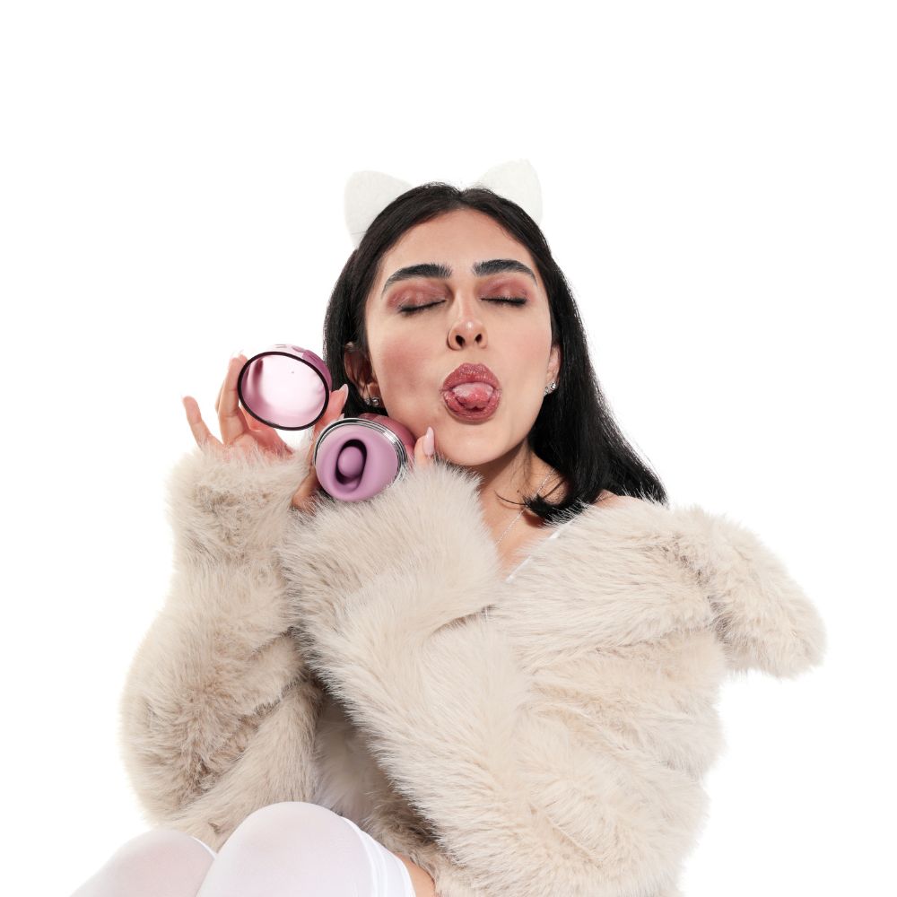 Woman holding the opened Svakom Klitty Interactive Licking, Sucking & Vibrating Clitoral Stimulator beside her face, showing the suction mouth and playful cat-inspired styling.