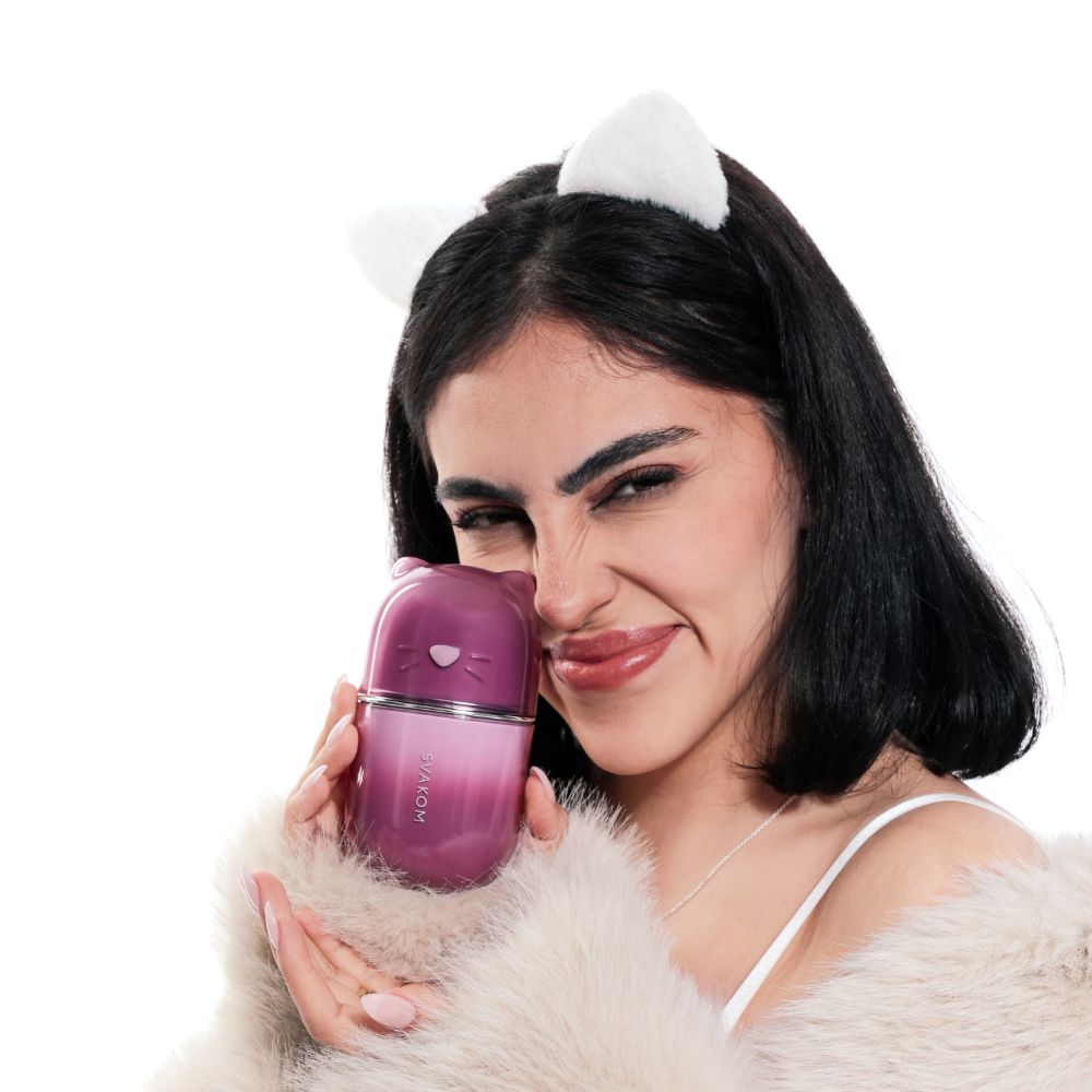 Woman posing with the Svakom Klitty Interactive Licking, Sucking & Vibrating Clitoral Stimulator held against her cheek, showing the front of the product and its cat-inspired shape.
