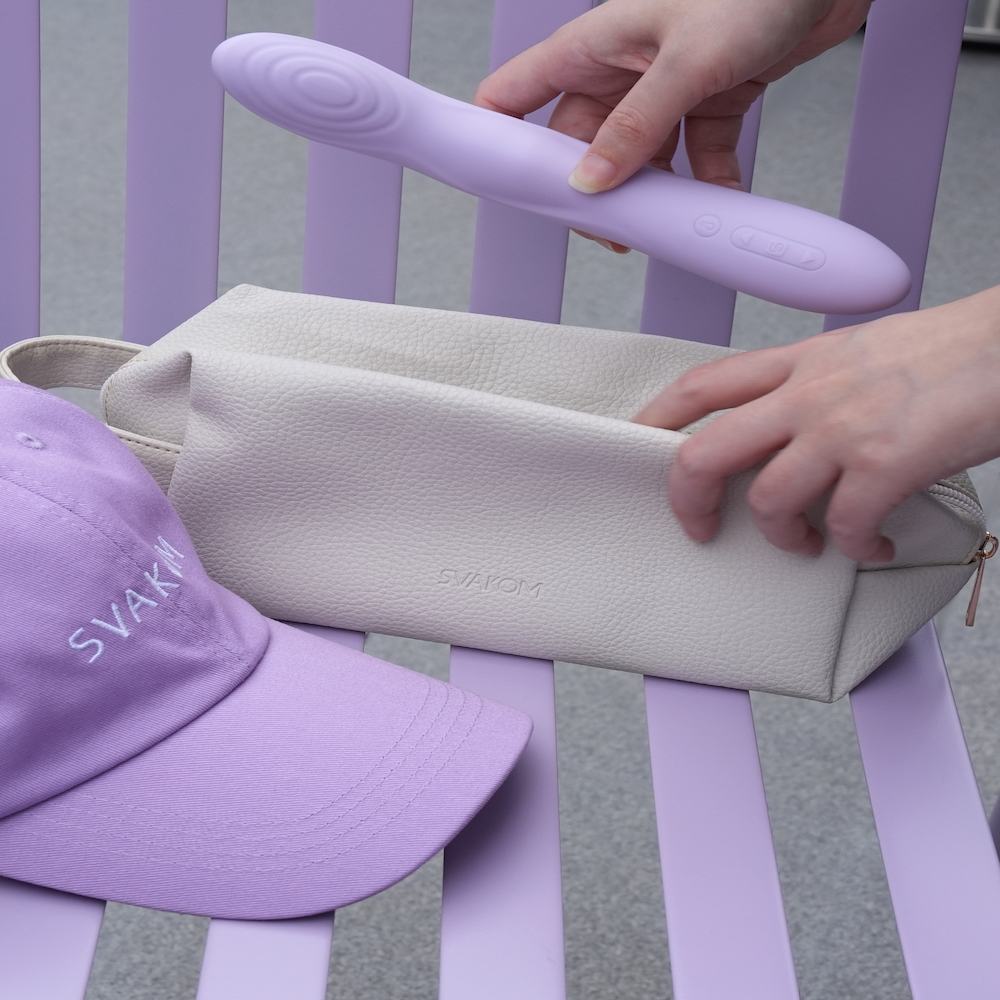 Person holding the Svakom Selena App-Controlled Heating & Thrusting G-Spot Vibrator next to a purple cap on a striped background