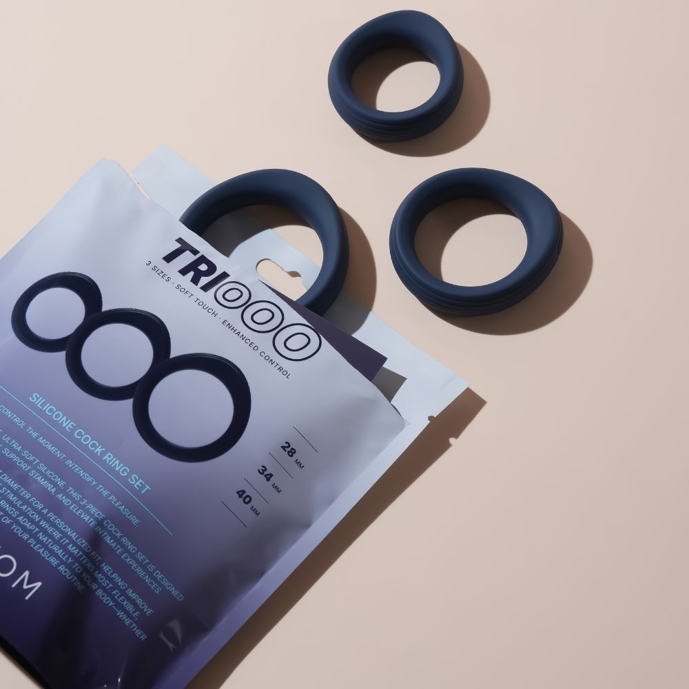 Svakom Triooo Three-Piece Silicone Cock Ring Set displayed with the product packaging and three dark blue rings on a beige surface.
