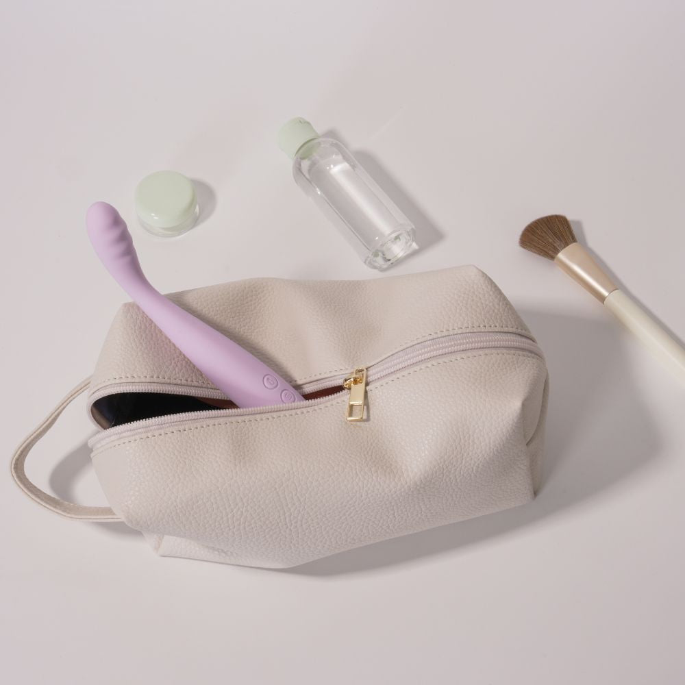 Svakom | Vegan Leather Storage Bag with Carry Handle (Beige) partially unzipped with a lilac vibrator inside, surrounded by a cosmetic jar, clear bottle and makeup brush on a soft neutral background