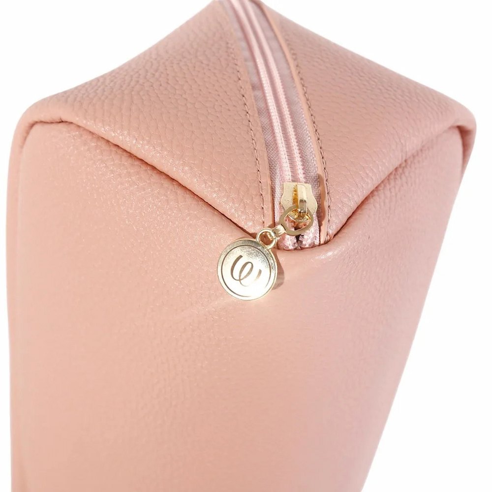 A close-up of the blush pink Womanizer Cosmetic Toy Bag, featuring a gold-tone metal zipper and a round gold-tone logo charm
